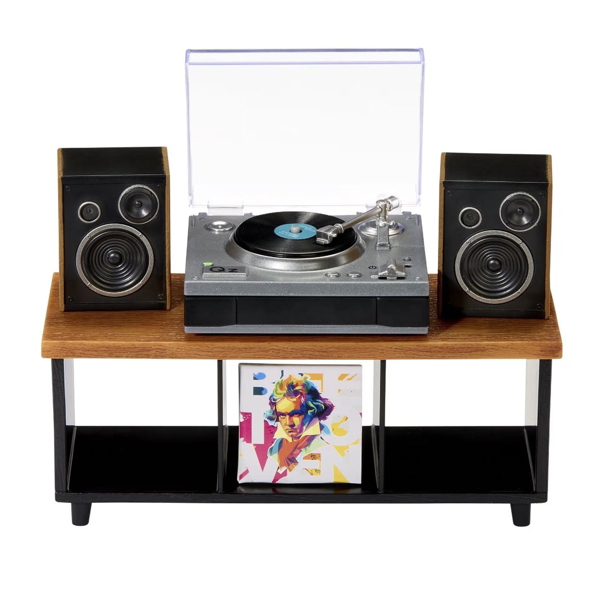 A retro-style record player console with a wooden top shelf, black metal legs, two black speakers, a silver and black turntable with a clear dust cover open, and a vinyl record on the platter. A framed colorful art print hangs below on a white background.