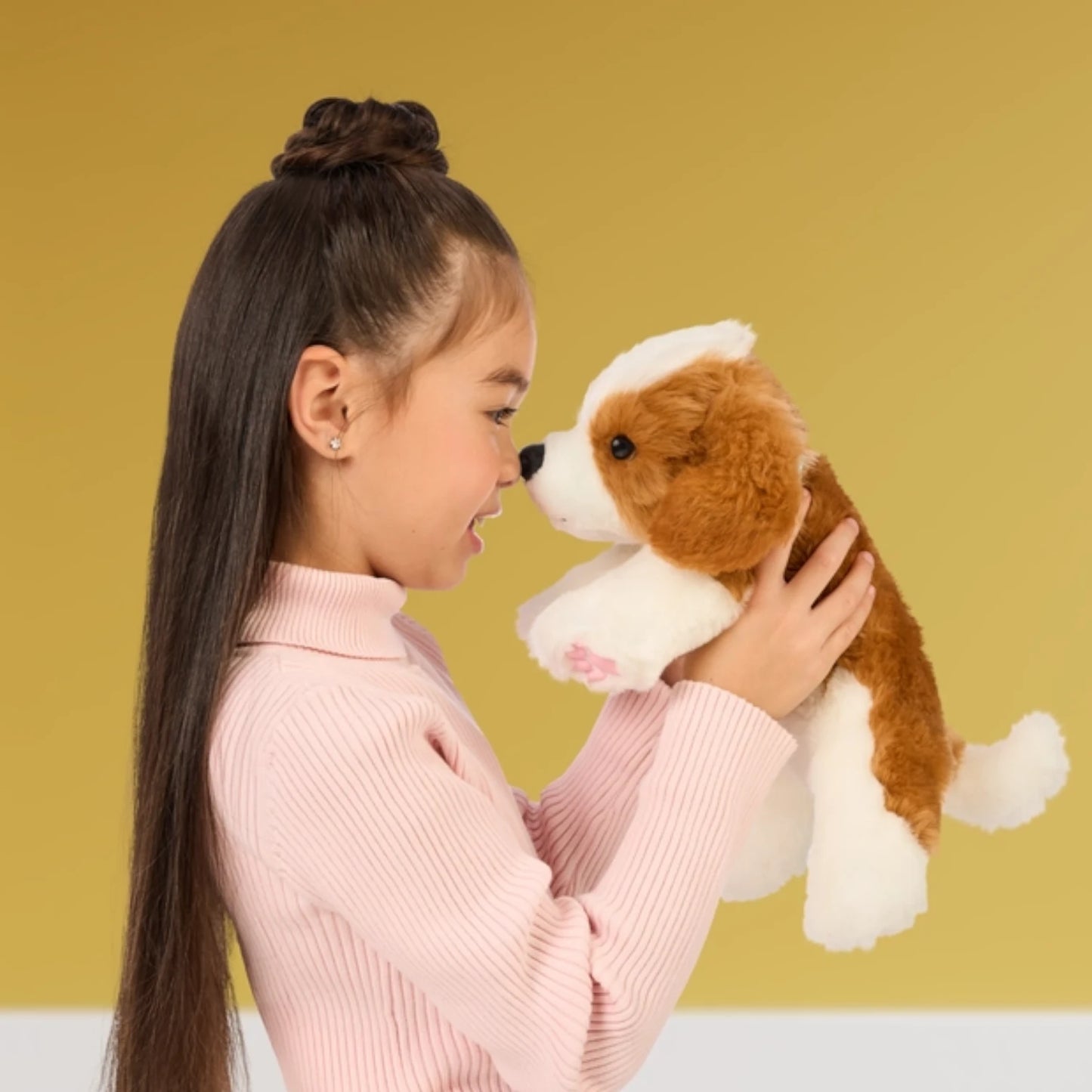 Young girl holding a brown and white stuffed dog toy against a yellow background