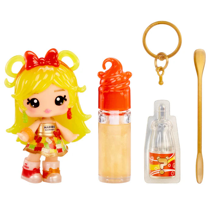 Yummiland x Haribo Goldbears lip gloss doll with yellow hair, a dress featuring gummy bear print, and red boots, shown with DIY lip gloss kit components including gold lip gloss tube, scented liquid packet, stirring spoon, and keychain ring.