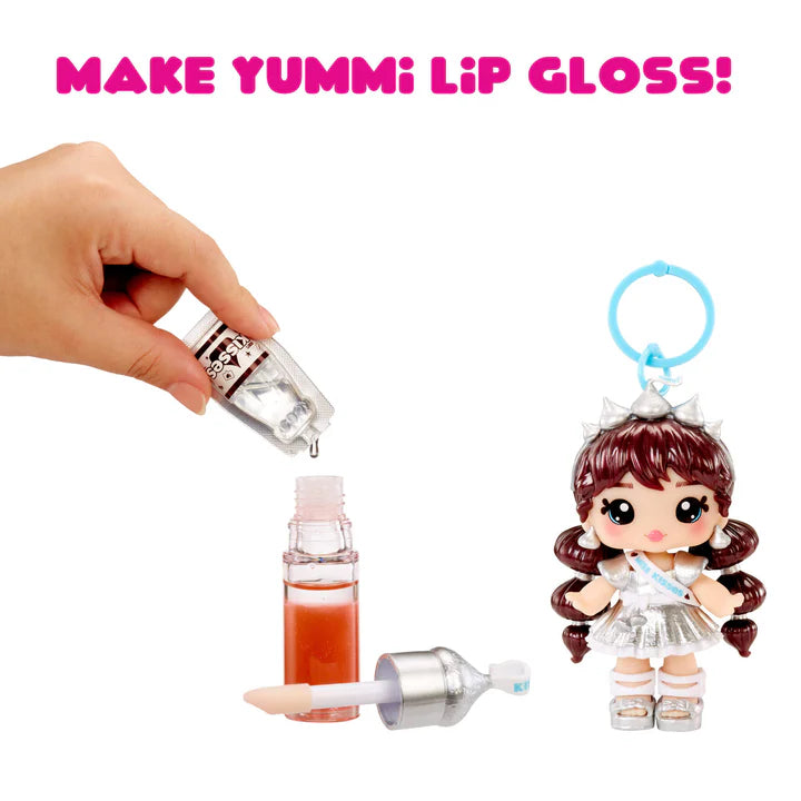 Make Yummi lip gloss kit with a hand holding a dropper, a small bottle of lip gloss, and a doll keychain on a white background.