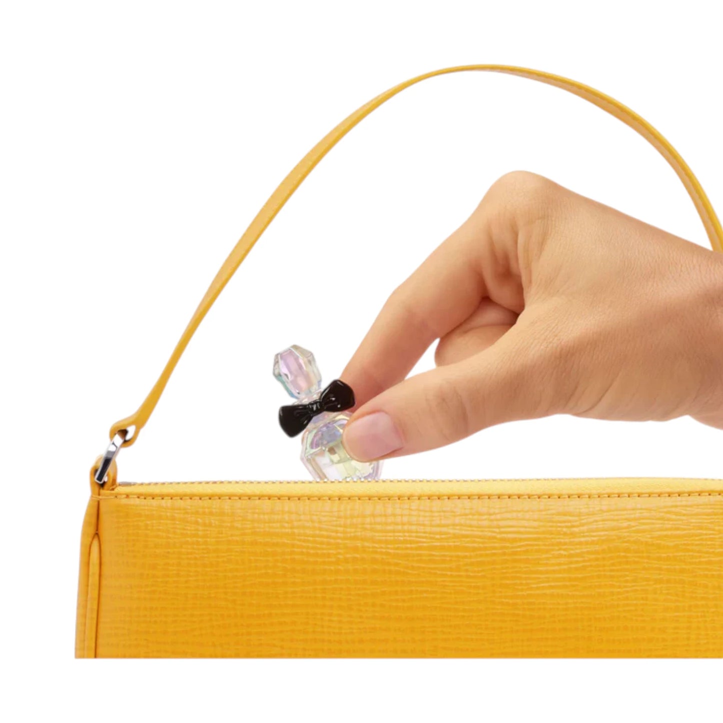 Hand holding a small Miniverse Make It Mini Fragrances near a yellow handbag on a white background