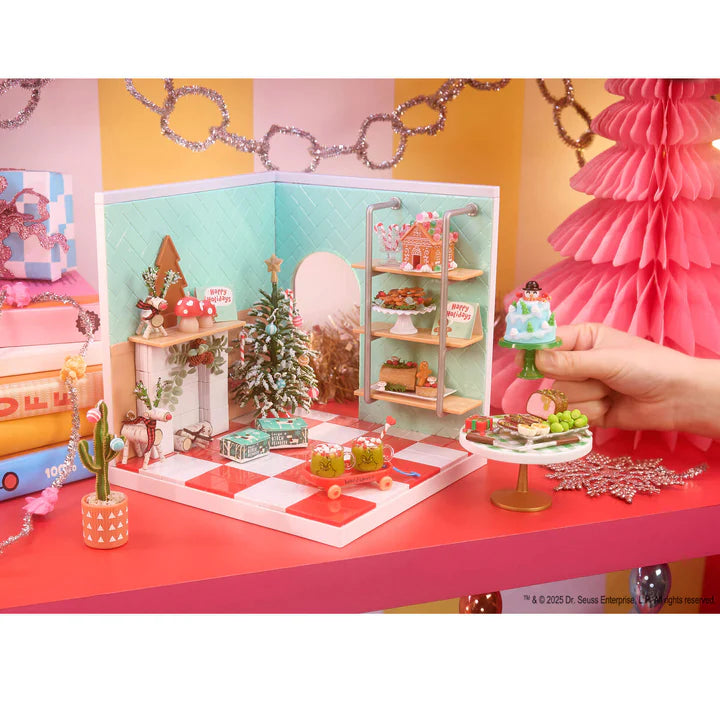 Miniature Christmas scene with a hand holding a small cake, surrounded by festive decorations on a colorful background.
