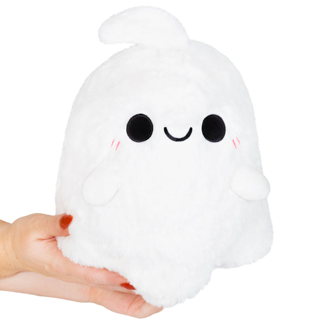 Squishable Mini Spooky Ghost White plush ghost toy with a smiling face held in a hand on a white background