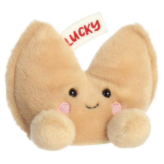 Aurora Palm Pals Lucky Fortune Cookie plush food character featuring golden-brown fur, an embroidered fortune slip reading LUCKY, and rosy cheeks sitting upright.