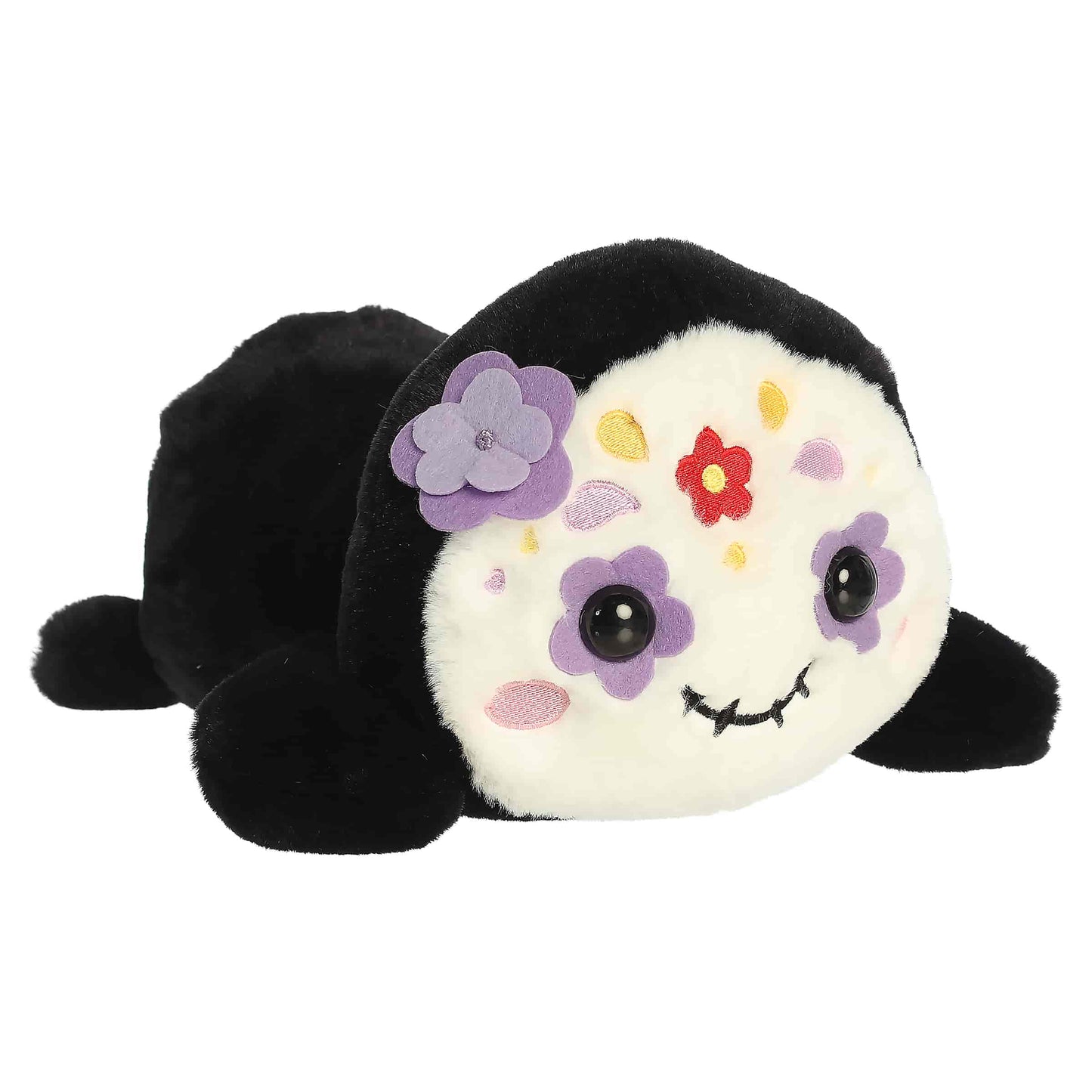 Aurora Too Cute Sissy Sugar Skull plush lying belly-down featuring a white face with colorful embroidered floral patterns and a purple 3D flower.