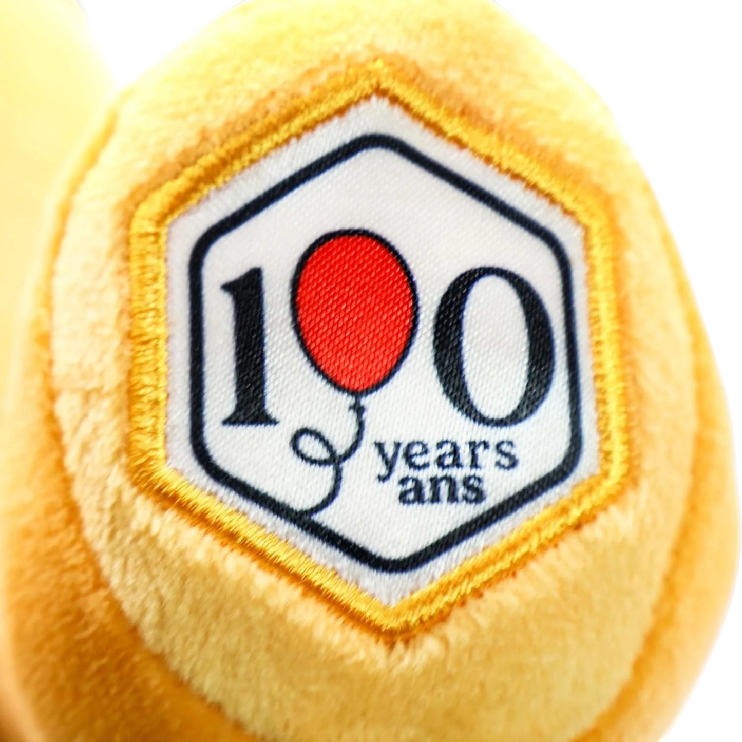 Yellow plush ball with a '100 years ans' patch featuring a red balloon.