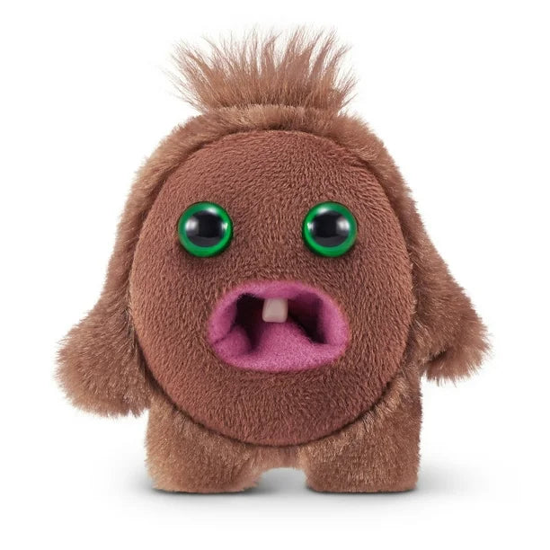 A small, roundish brown Fuggler Baby Fugg plush toy (Hedge Grog) with large green eyes, two white baby teeth showing in a pink mouth, and a spiky brown tuft of hair on top.