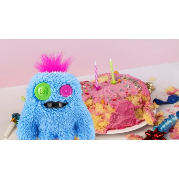 Blue plush toy with pink hair next to a colorful birthday cake on a white plate with a pink background.