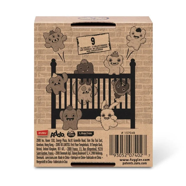 Back of display box for A small, shaggy blue Fuggler Baby Fugg plush toy (SaBQuoosh) with mismatched button eyes (one green, one pink), two white baby teeth showing, and a spiky pink tuft of hair on top.