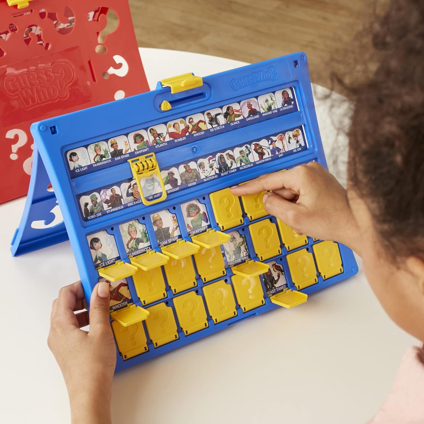 Child playing with a board game featuring character cards on a white surface.