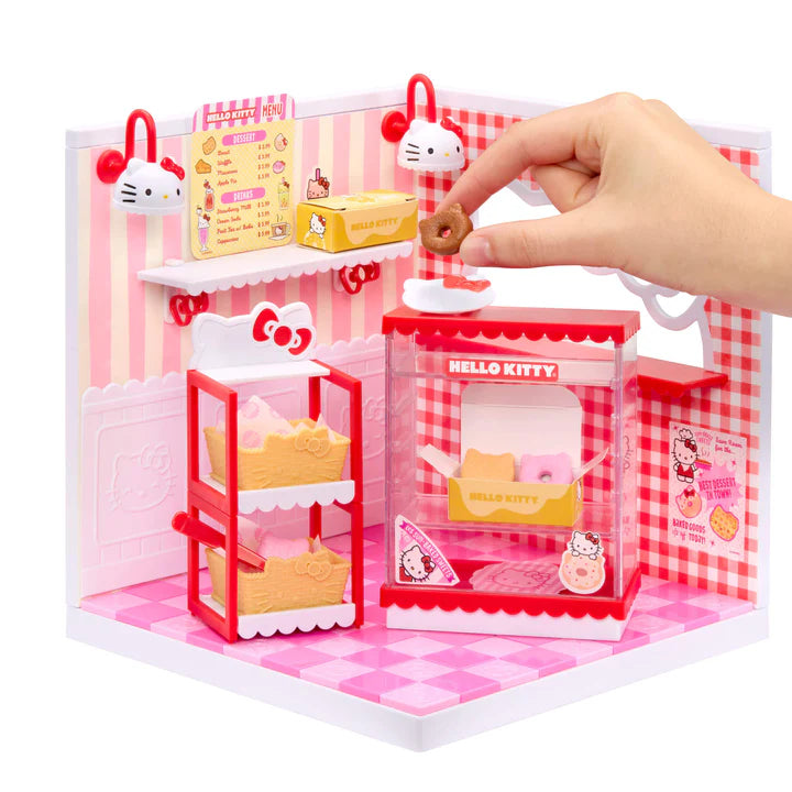 MGA Miniverse Make It Mini Spaces Hello Kitty miniature playset with pink panels and accessories with a hand interacting with it on a white background