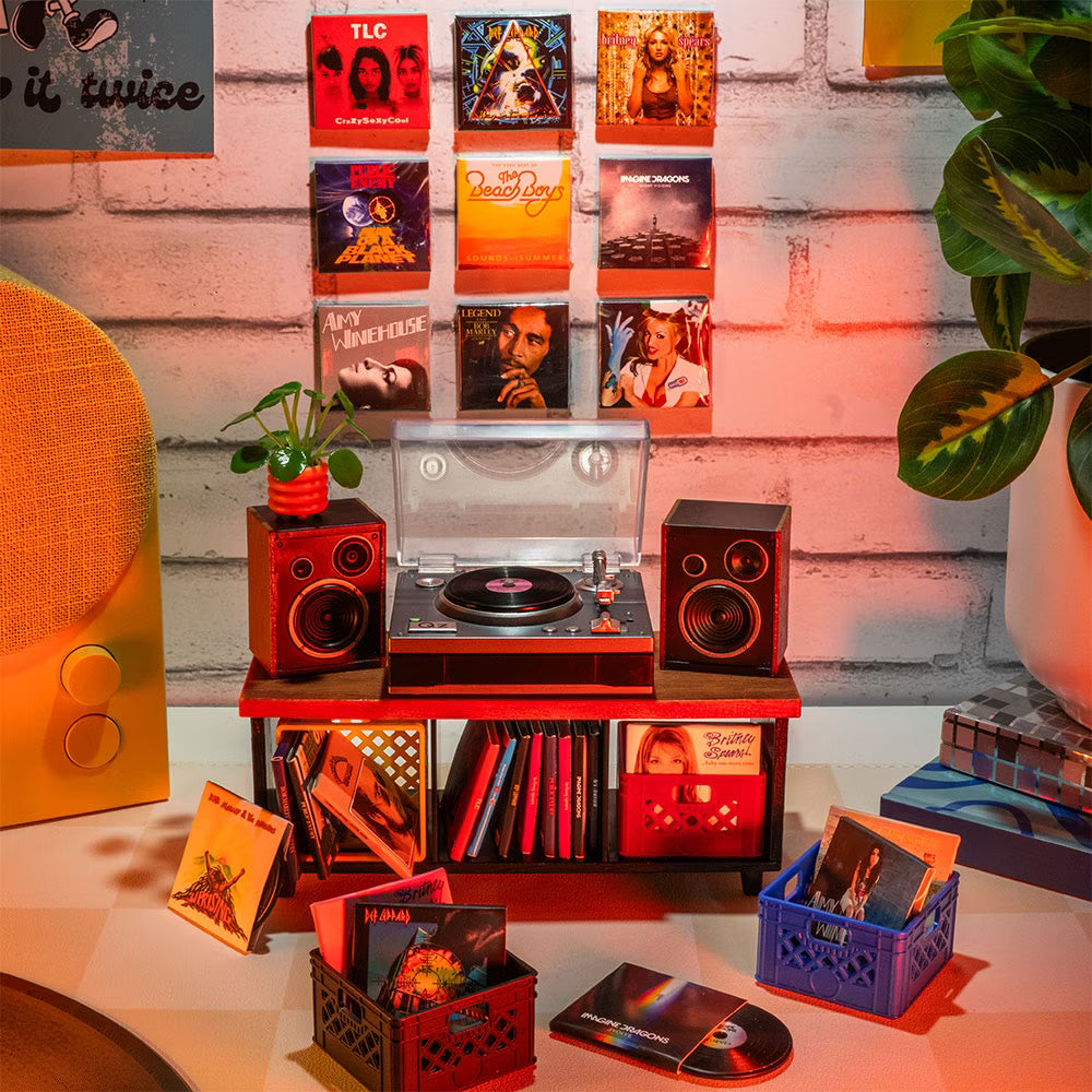 A hot pink mystery blind pack ball for MGA's Miniverse Real Music Vinyl surrounded by mini playable vinyl records, sleeves, and crates.