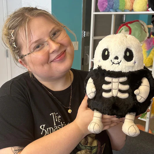 Woman holding Mini Squishable Skeleton plush with stitched grin and embroidered bones