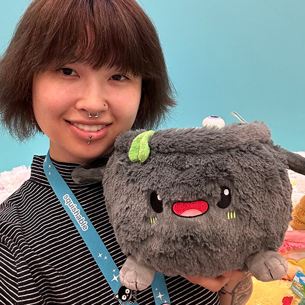 Person holding a Squishable Mini Cauldron plush toy with a blue background