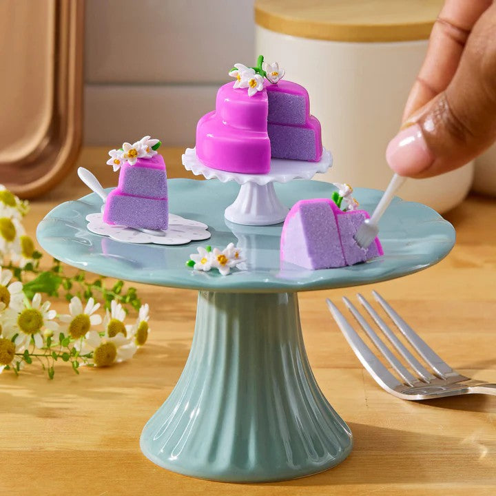 Miniature purple cake with white flowers on a small green stand, with a hand holding a fork. Miniverse Make It Mini From Scratch Series 2