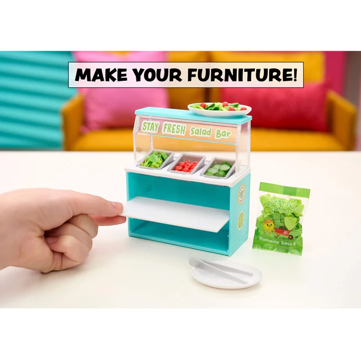 Miniature salad bar with a hand interacting with it, set against a colorful background. Miniverse Make it Mini Spaces Furniture.