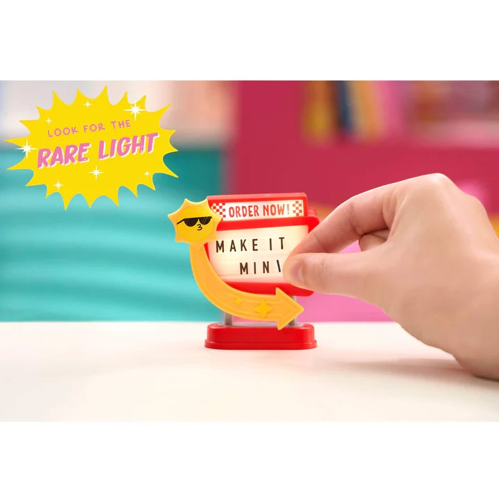 Hand interacting with a small light-up sign with text on a colorful background. Miniverse Make it Mini Spaces Furniture.