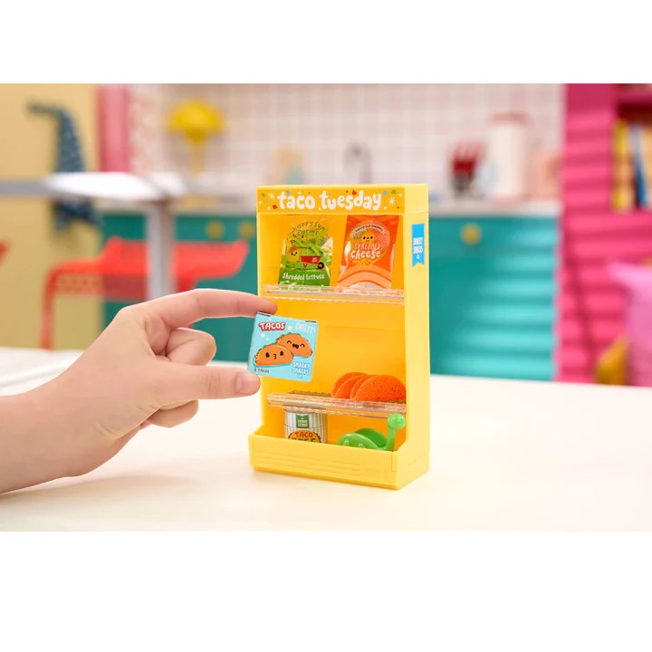 Hand holding a yellow packaging of Taco Tuesday with a colorful classroom background. Miniverse Make it Mini Spaces Furniture.
