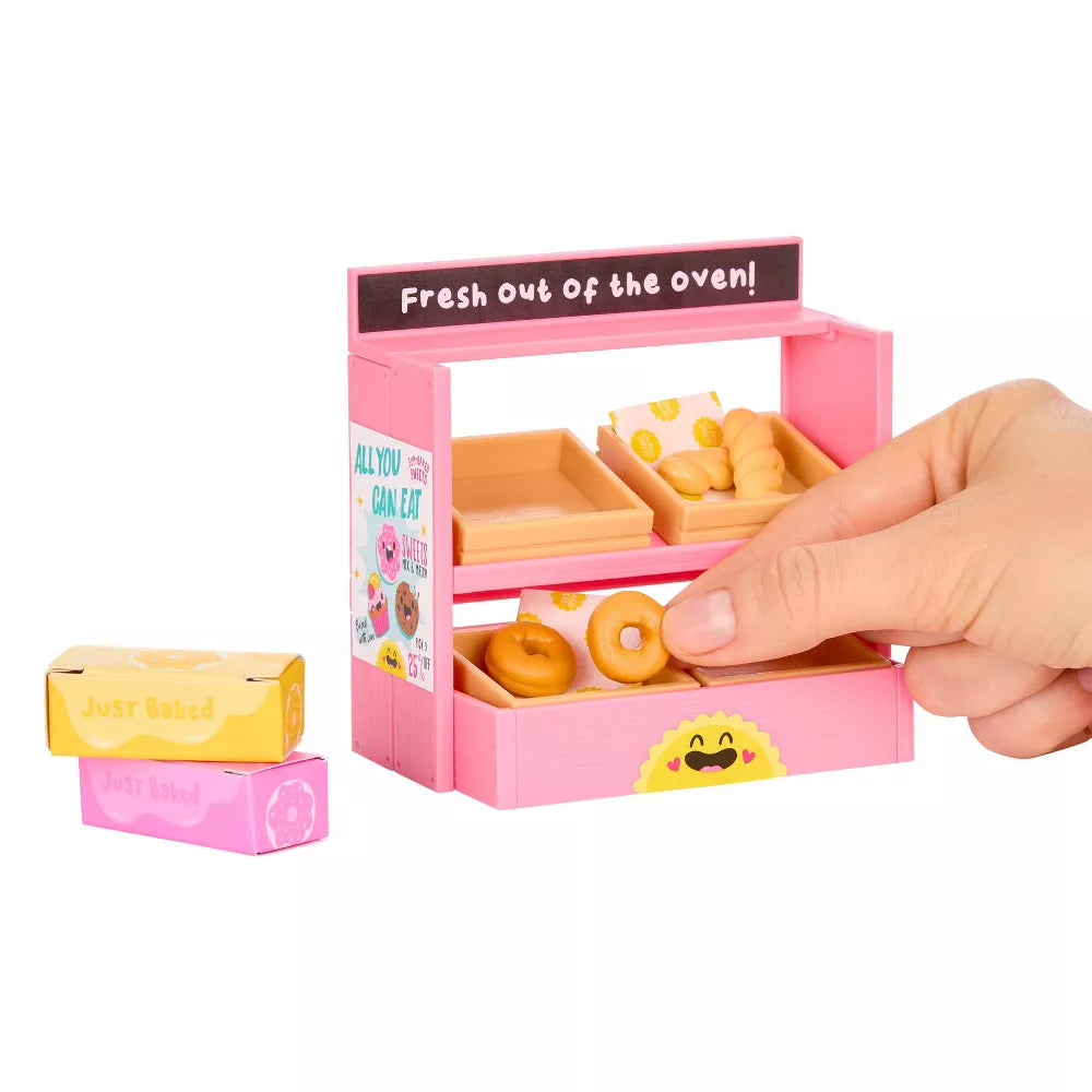 Miniverse Make It Mini Spaces Furniture Small pink toy bakery with donuts and a hand interacting with it on a white background