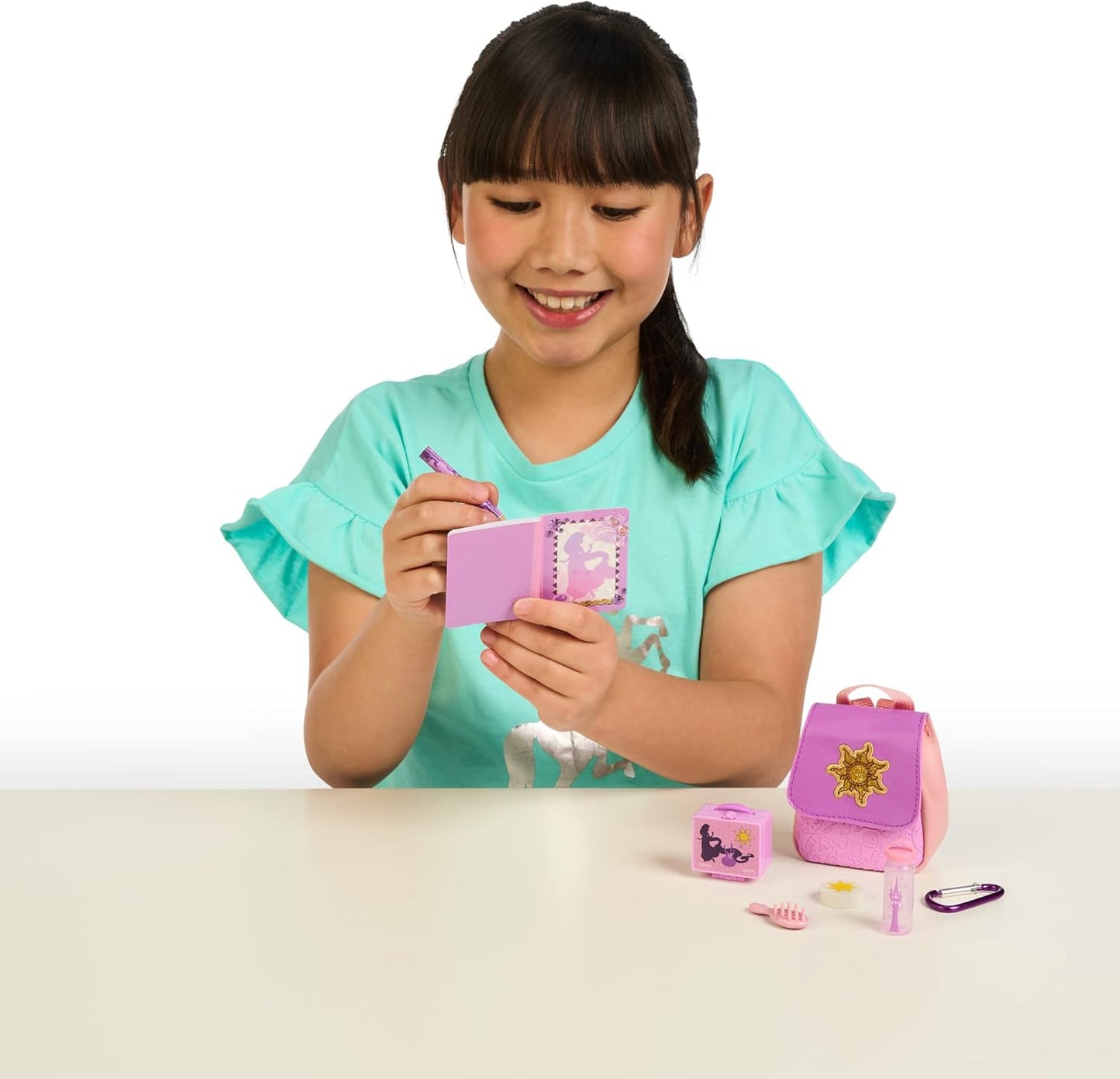 Young girl holding a pink toy wallet with accessories on a white background
