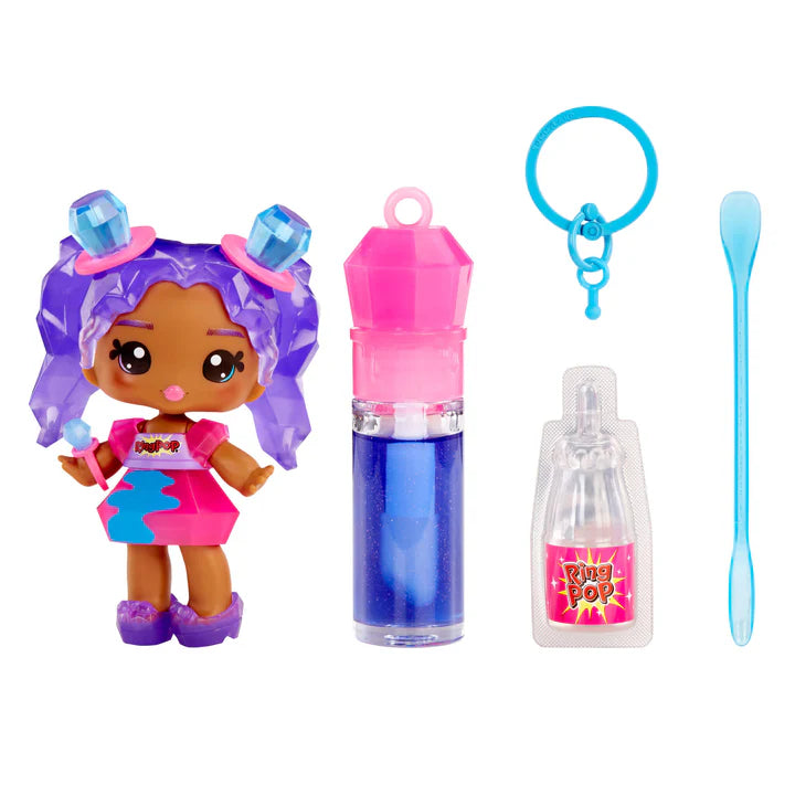 Yummiland x Ring Pop lip gloss doll with purple hair featuring gemstone accents, wearing a pink dress, shown with DIY lip gloss kit components including blue lip gloss tube, scented liquid packet, stirring spoon, and keychain ring.