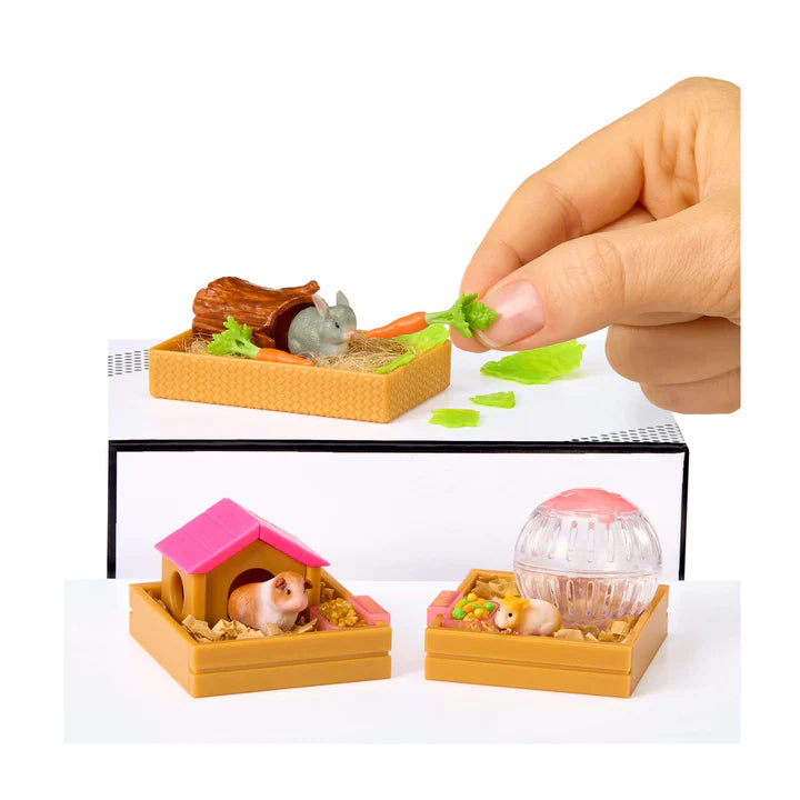 Miniature pet playset with small animals and accessories, including a hand holding food from Miniverse Make It Mini Animals surprise capsule.