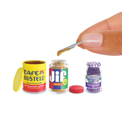 Miniature jars of Cafe Bustelo coffee, Jif peanut butter, and Smucker's grape jelly with a hand holding a spoon.