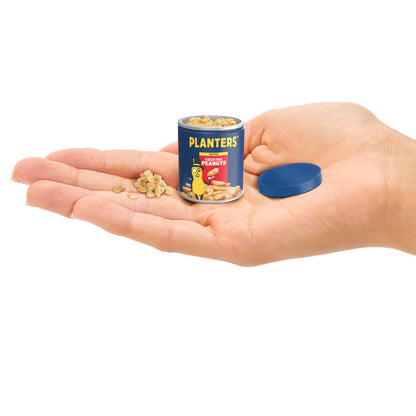 Miniature can of Planters peanuts held in a hand with scattered peanuts on a white background