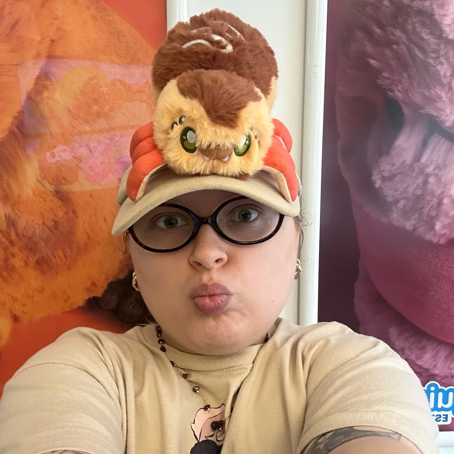 Person wearing a cap with a plush toy on top, making a playful face in front of colorful background