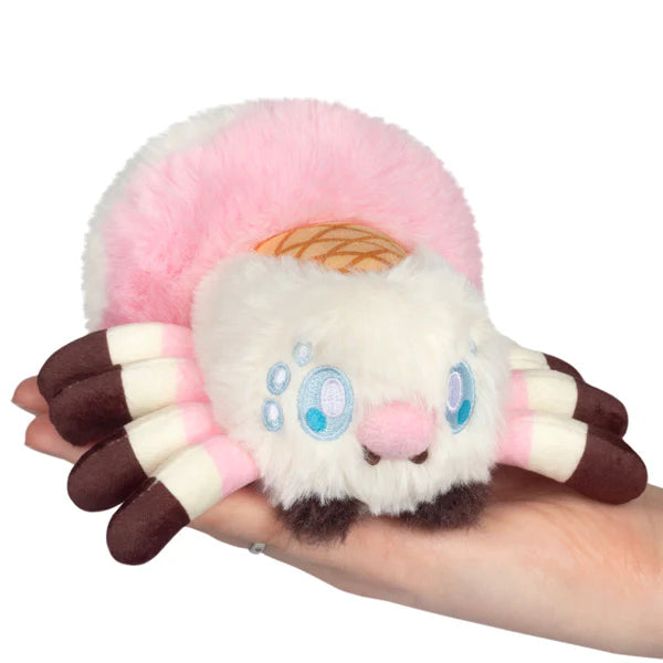 Squishable Alter Egos Series 20 Ice Cream Spider plush held in a hand, featuring fluffy white and pink fur, a waffle cone detail, and brown striped legs.