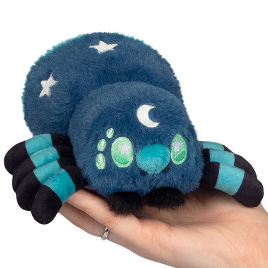 Squishable Alter Egos Series 20 Midnight Spider plush held in a hand, featuring deep blue fur, light blue striped legs, green eyes, and white moon and star details.