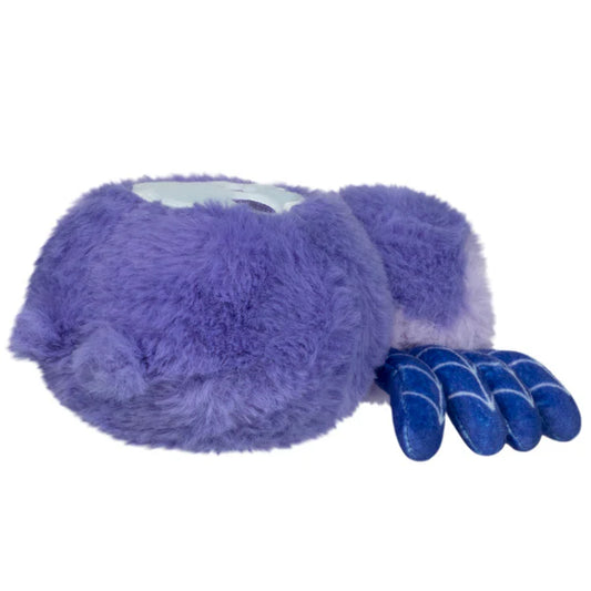 Squishable Alter Egos Series 20 Skull Spider plush held in a hand, featuring soft purple fur, pink eyes, blue web-patterned legs, and a skull printed on its back.