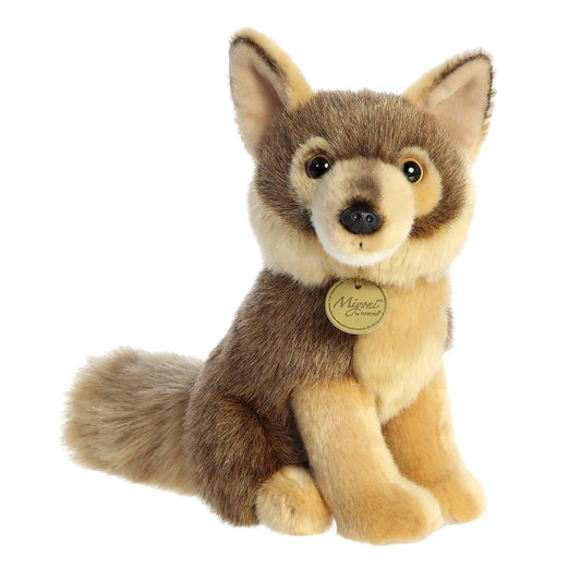 A product photo of the Aurora Miyoni Coyote 9.5-Inch Plush, a light and dark brown realistic coyote stuffed animal in a sitting pose, wearing a gold Miyoni tag.