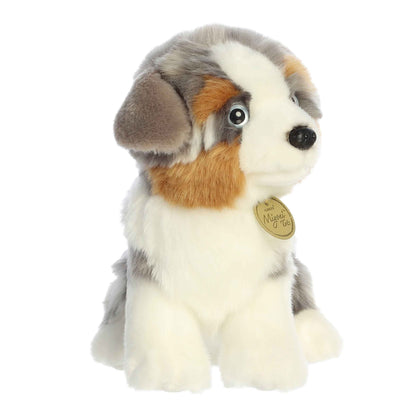 Aurora Miyoni Tots Australian Shepherd Pup lifelike baby plush stuffed animal sitting with a multi-colored black, white, and tan coat and expressive eyes.