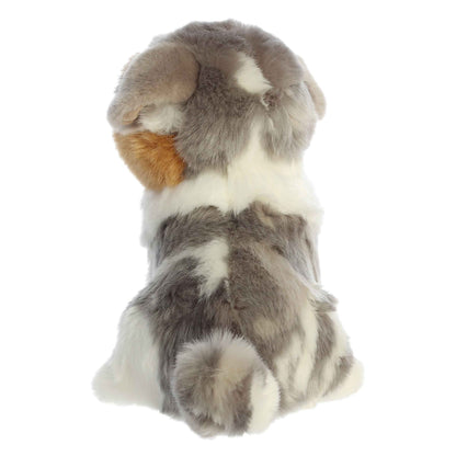 Aurora Miyoni Tots Australian Shepherd Pup lifelike baby plush stuffed animal sitting with a multi-colored black, white, and tan coat and expressive eyes.