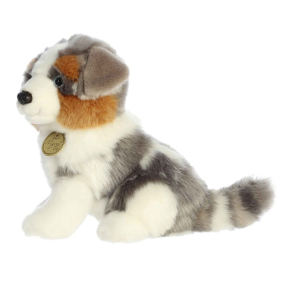 Aurora Miyoni Tots Australian Shepherd Pup lifelike baby plush stuffed animal sitting with a multi-colored black, white, and tan coat and expressive eyes.