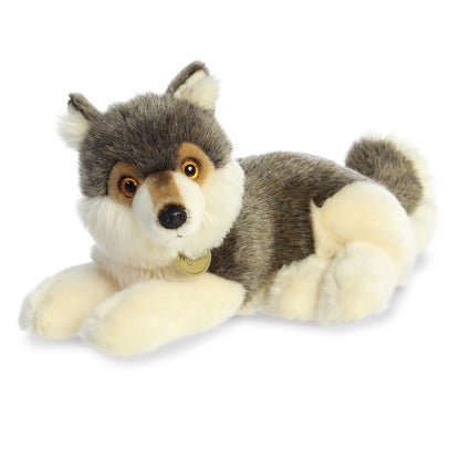 A product photo of the Aurora Miyoni Wolf 15-Inch Plush, a gray and brown wolf stuffed animal lying down with a realistic pose and amber eyes, wearing a small tag.
