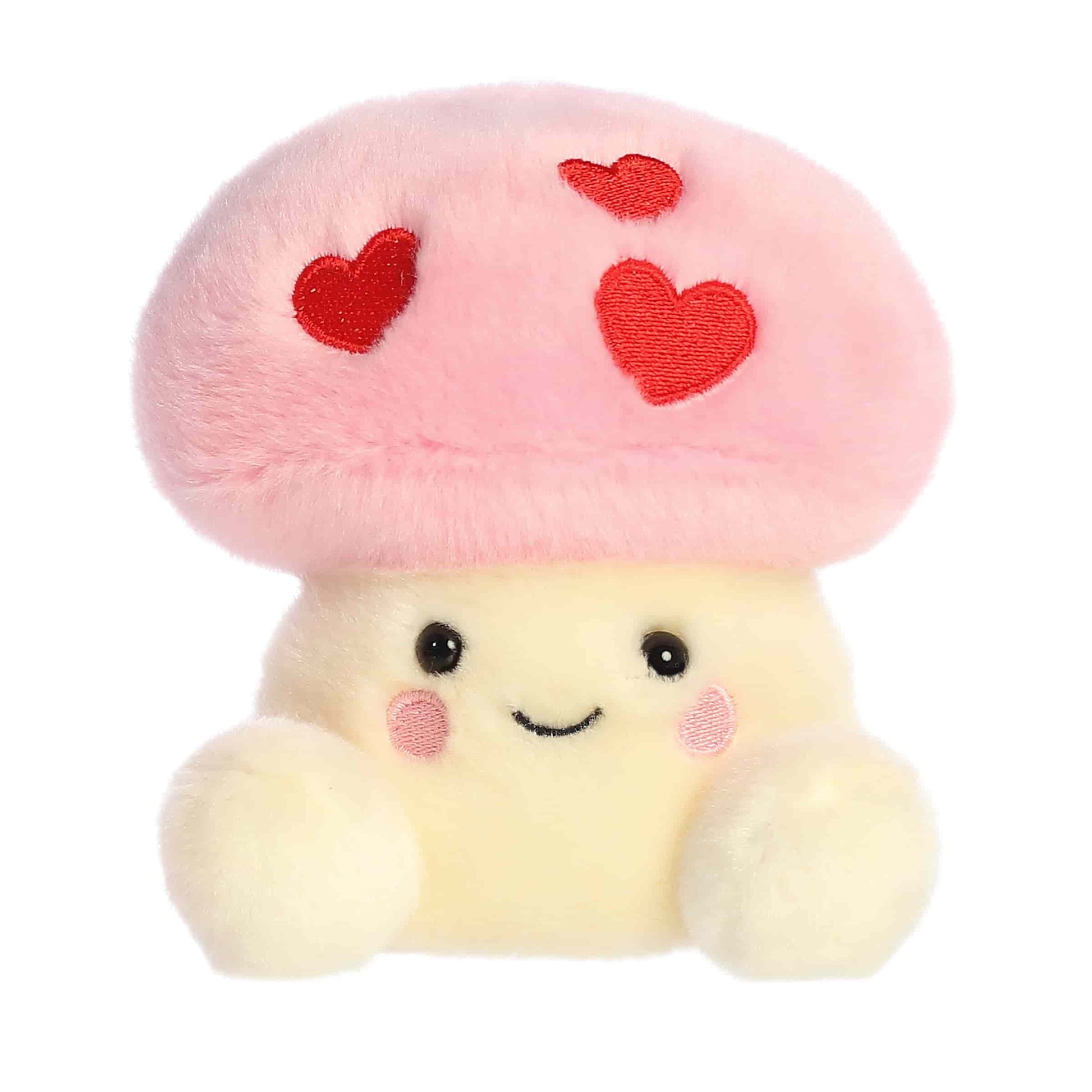 Product view of Aurora Palm Pals Brooklyn Mushroom, a small plush mushroom with a pink cap featuring three embroidered red hearts.