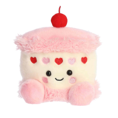Product view of Aurora Palm Pals Jubi Heart Cake, a small plush cake with pink frosting, heart sprinkles, and a cherry on top.