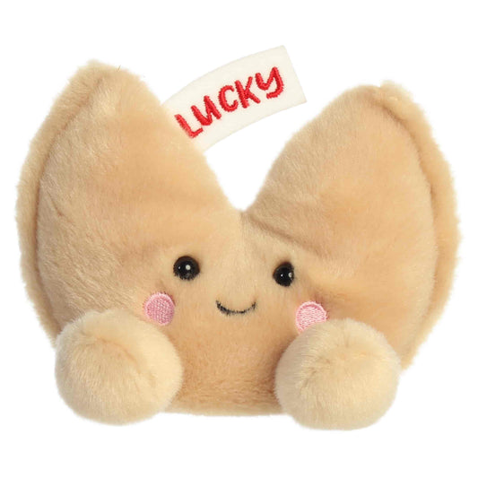 Aurora Palm Pals Lucky Fortune Cookie plush food character featuring golden-brown fur, an embroidered fortune slip reading LUCKY, and rosy cheeks sitting upright.