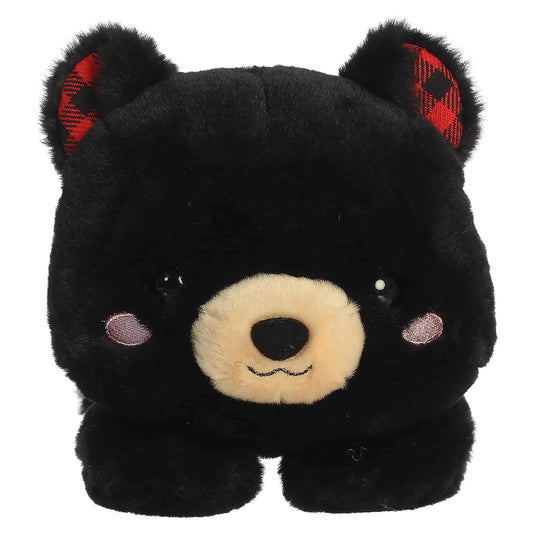 Aurora Too Cute Ben Black Bear plush lying belly-down featuring soft black fur, a tan snout, rosy cheeks, and red buffalo plaid inner ears.