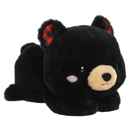 Aurora Too Cute Ben Black Bear plush lying belly-down featuring soft black fur, a tan snout, rosy cheeks, and red buffalo plaid inner ears.