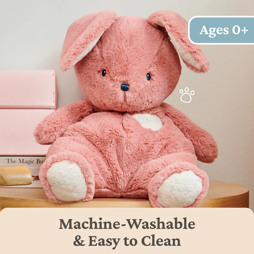 Pink plush toy with bunny ears on a wooden surface, with text indicating machine-washability.