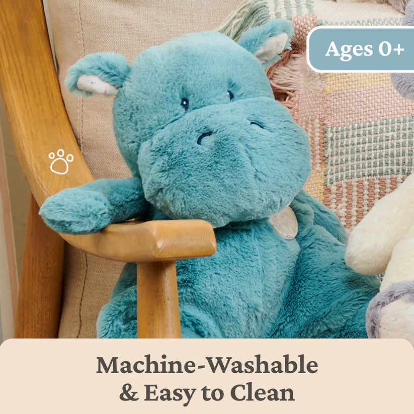 Blue plush toy hippo sitting on a wooden chair with text indicating it's machine-washable and easy to clean.