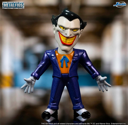 Metal-figs collectible figure of the Joker from The Batman, featuring a metallic purple suit, orange shirt, and white teeth, displayed against a blurred background.