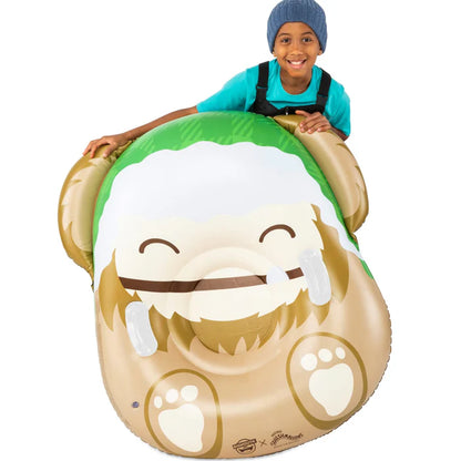 Child holding A large, inflatable snow tube designed to look like Benny the Big Foot Squishmallow, featuring his brown face, green plaid hat, and smiling mouth with one tooth