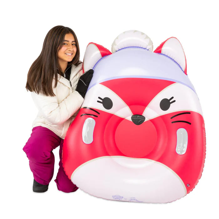 Woman holding a large, inflatable snow tube designed to look like Fifi the Fox Squishmallow, featuring her red and white fox face, a purple winter hat with a white pom-pom, and two sturdy side handles.