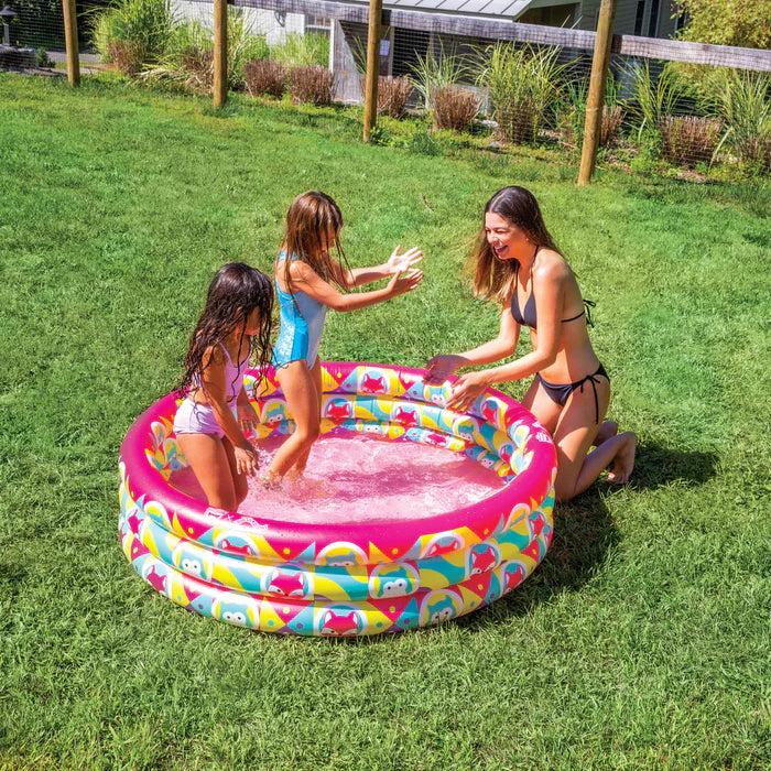 Three children playing in a colorful inflatable pool on a grassy lawn.