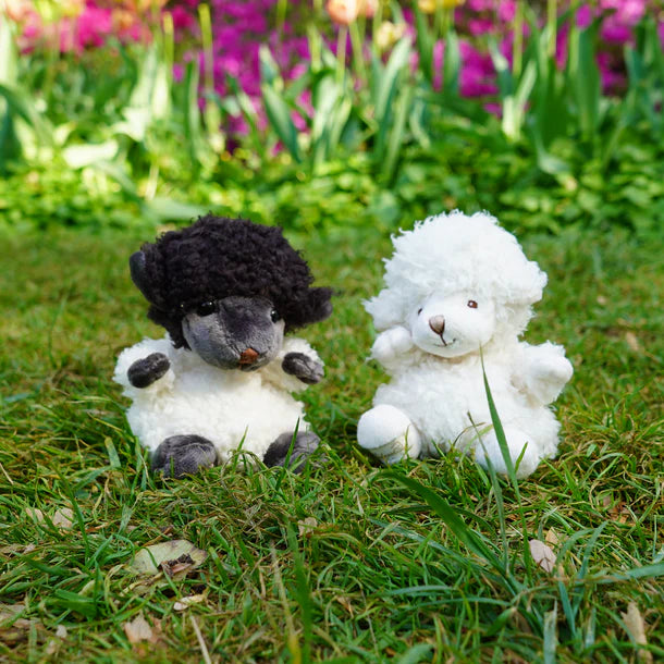 Two stuffed animals, one black and one white, sitting on grass with flowers in the background.