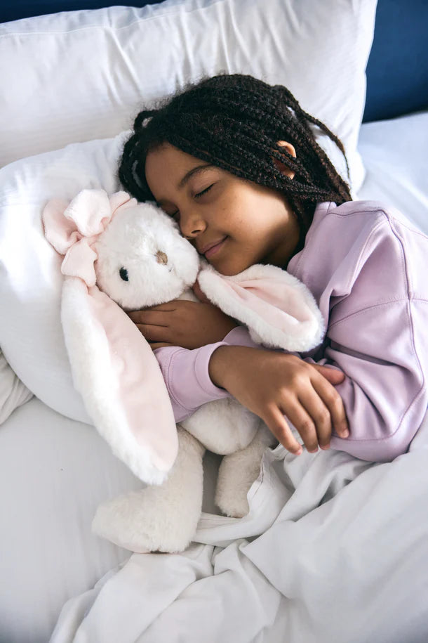 Child sleeping in bed with pink bunny plush toys